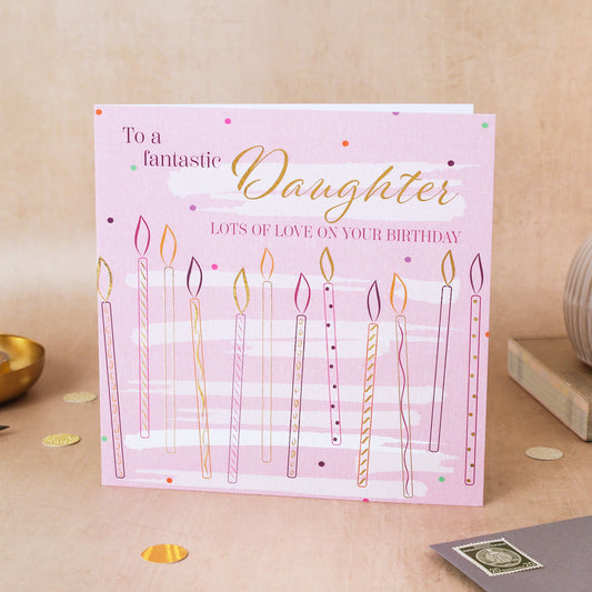 Birthday card for a daughter with candles on a pink background, placed on a wooden surface.