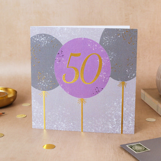 Greeting card with purple balloon featuring '50' on a beige surface
