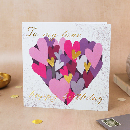 Greeting card with colorful hearts and 'Happy Birthday' text on a beige surface.