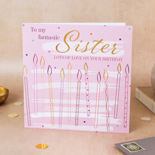 Birthday card for a sister with candles on a pink background, placed on a wooden surface.