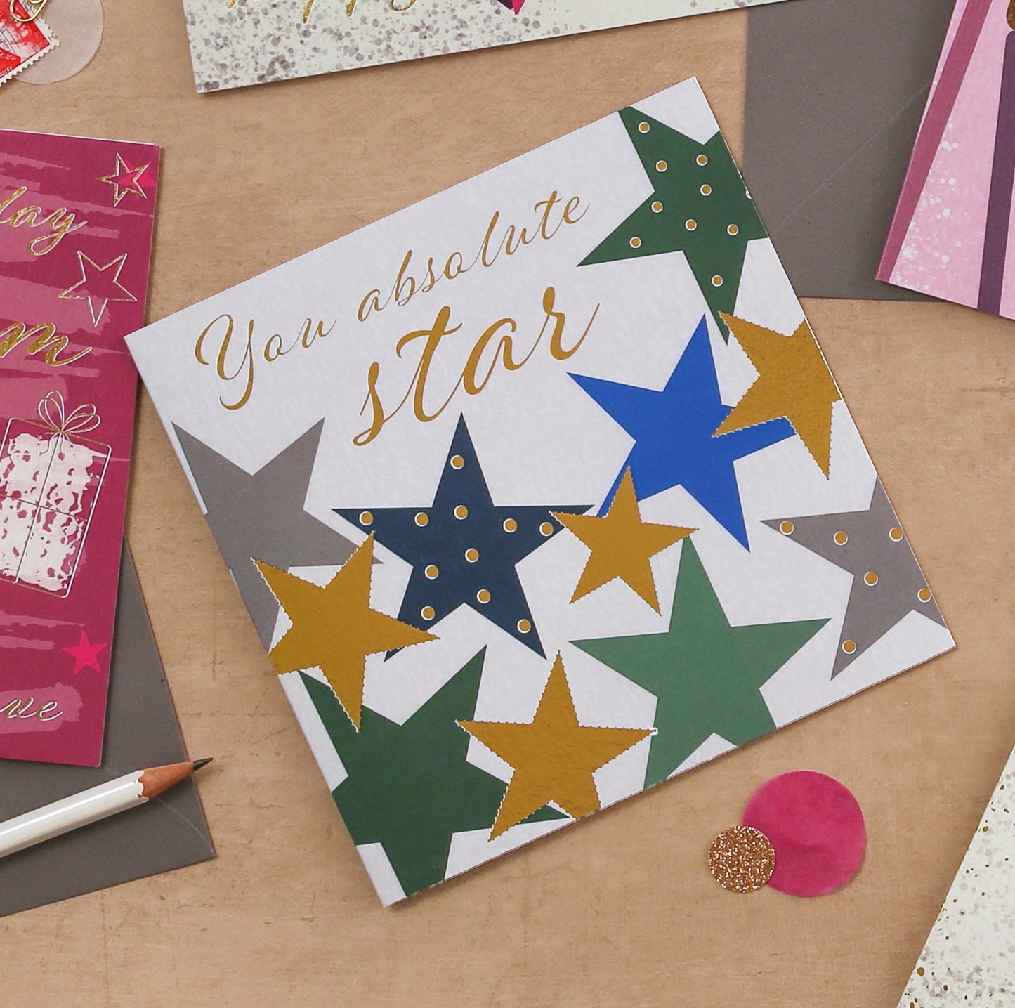 Card with colorful stars and text 'You absolute star' on a wooden surface with other cards and a pen.