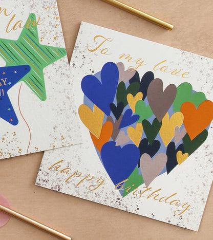Colorful heart-shaped birthday card on a beige surface with gold accents.