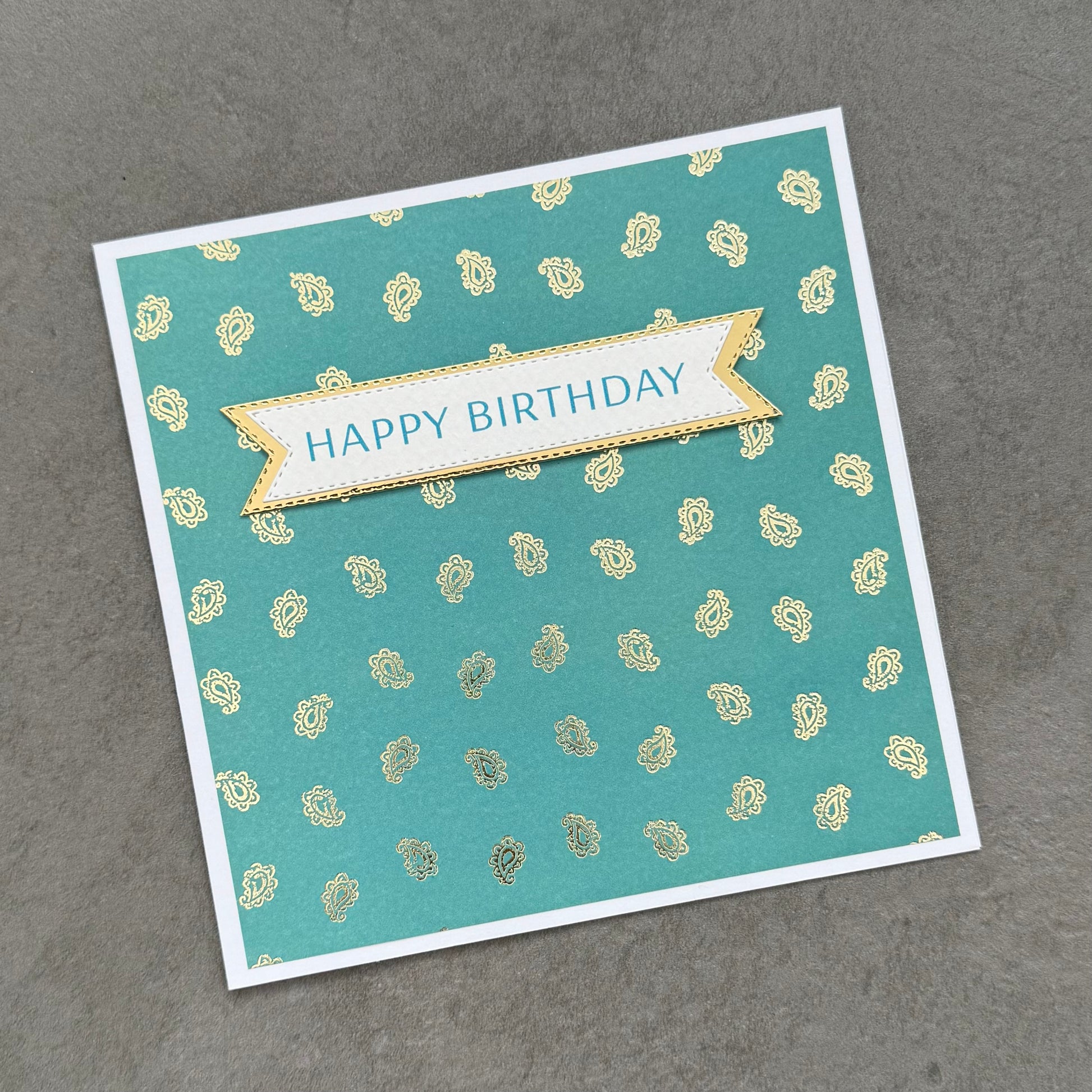 Birthday card with 'Happy Birthday' banner on a teal background with gold patterns
