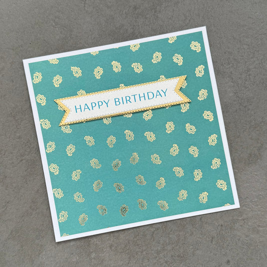 Birthday card with 'Happy Birthday' banner on a teal background with gold patterns