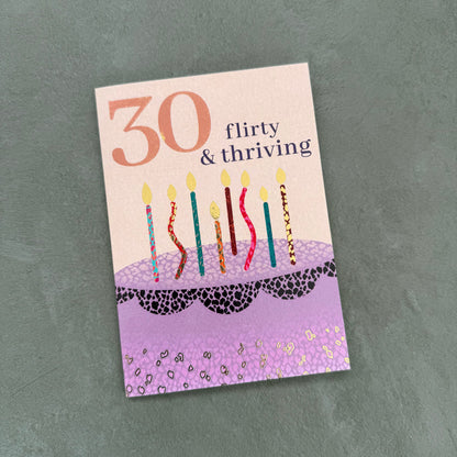 Birthday card with candles and text '30 flirty & thriving' on a textured gray background