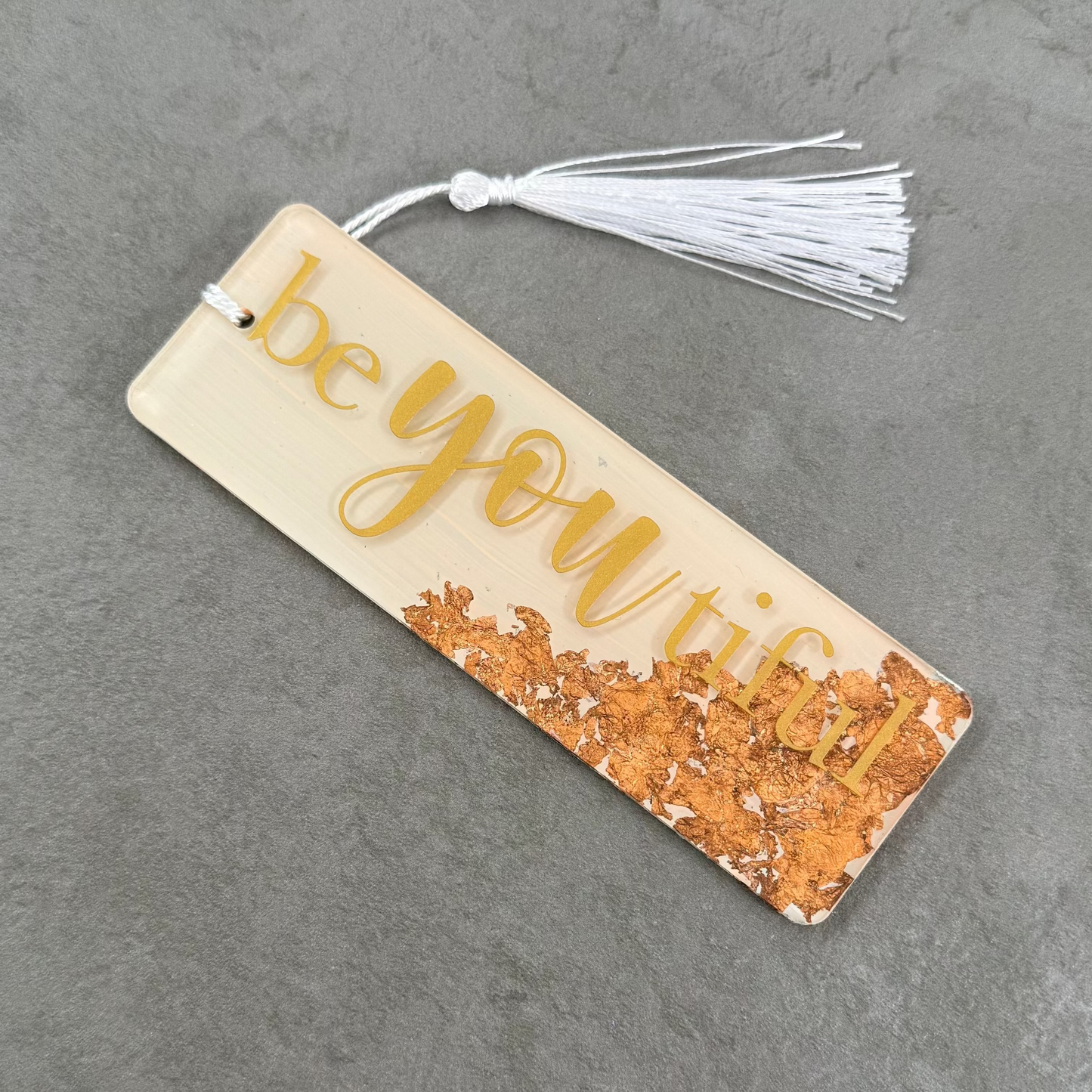 Bookmark with 'be you' text and tassel on a gray surface
