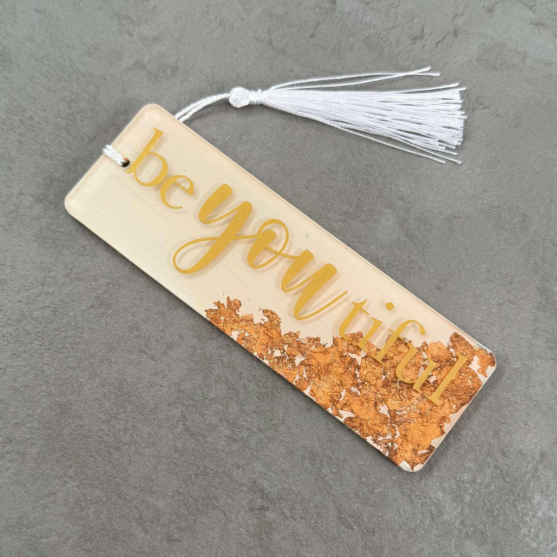 Bookmark with 'be you' text and tassel on a gray surface
