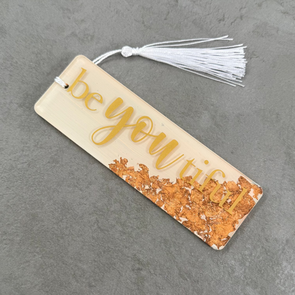 Bookmark with 'be you' text and tassel on a gray surface