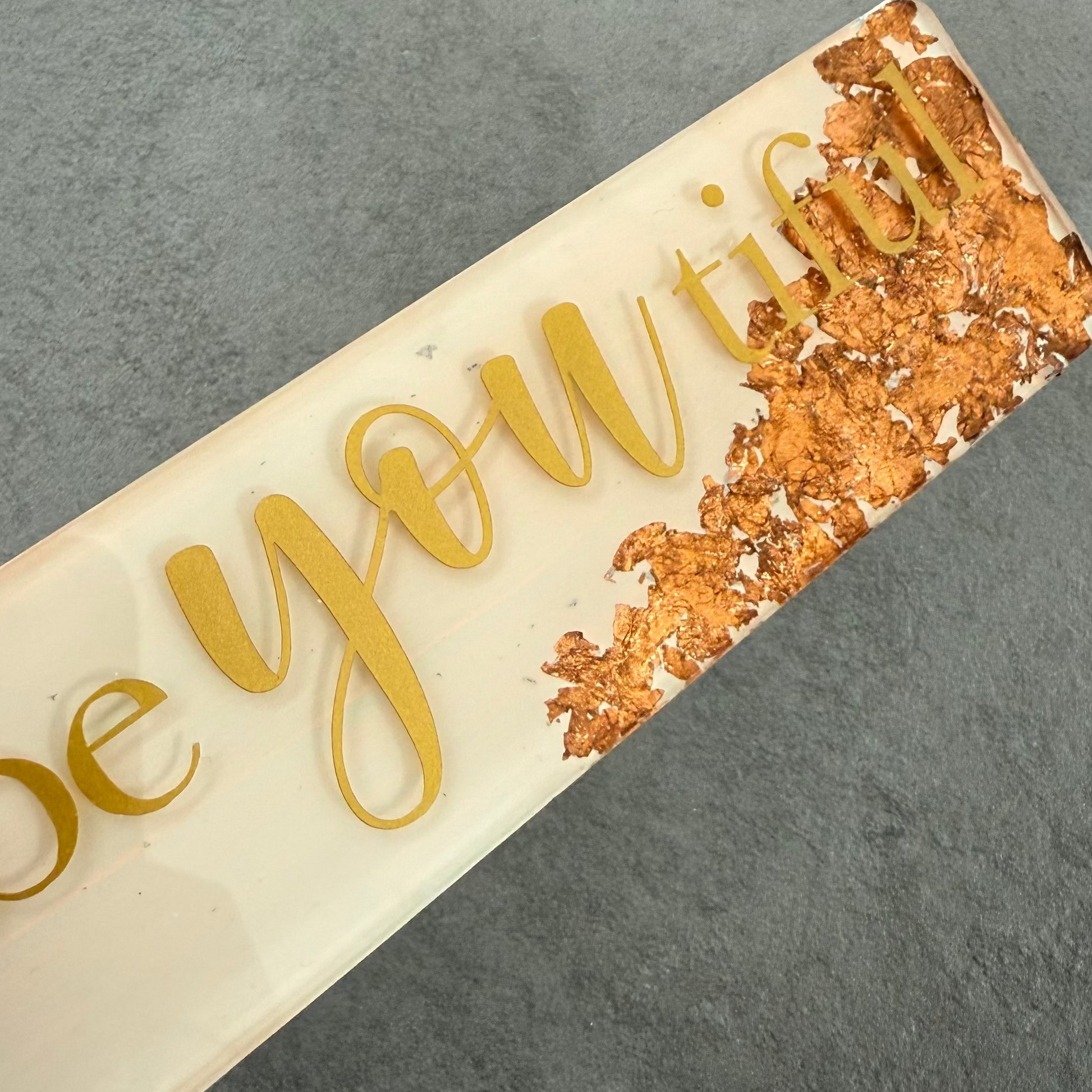 Decorative plaque with 'be you' text on a gray surface