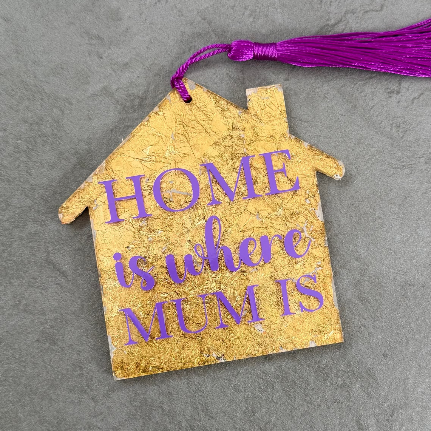 Decorative house-shaped tag with 'Home is where Mum is' text on a gray surface