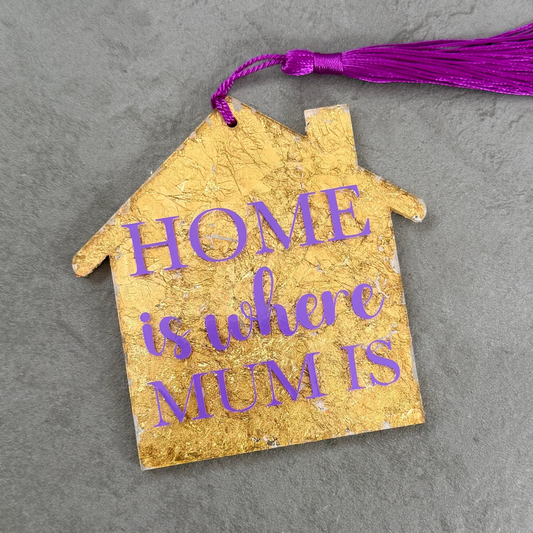 Decorative house-shaped tag with 'Home is where Mum is' text on a gray surface