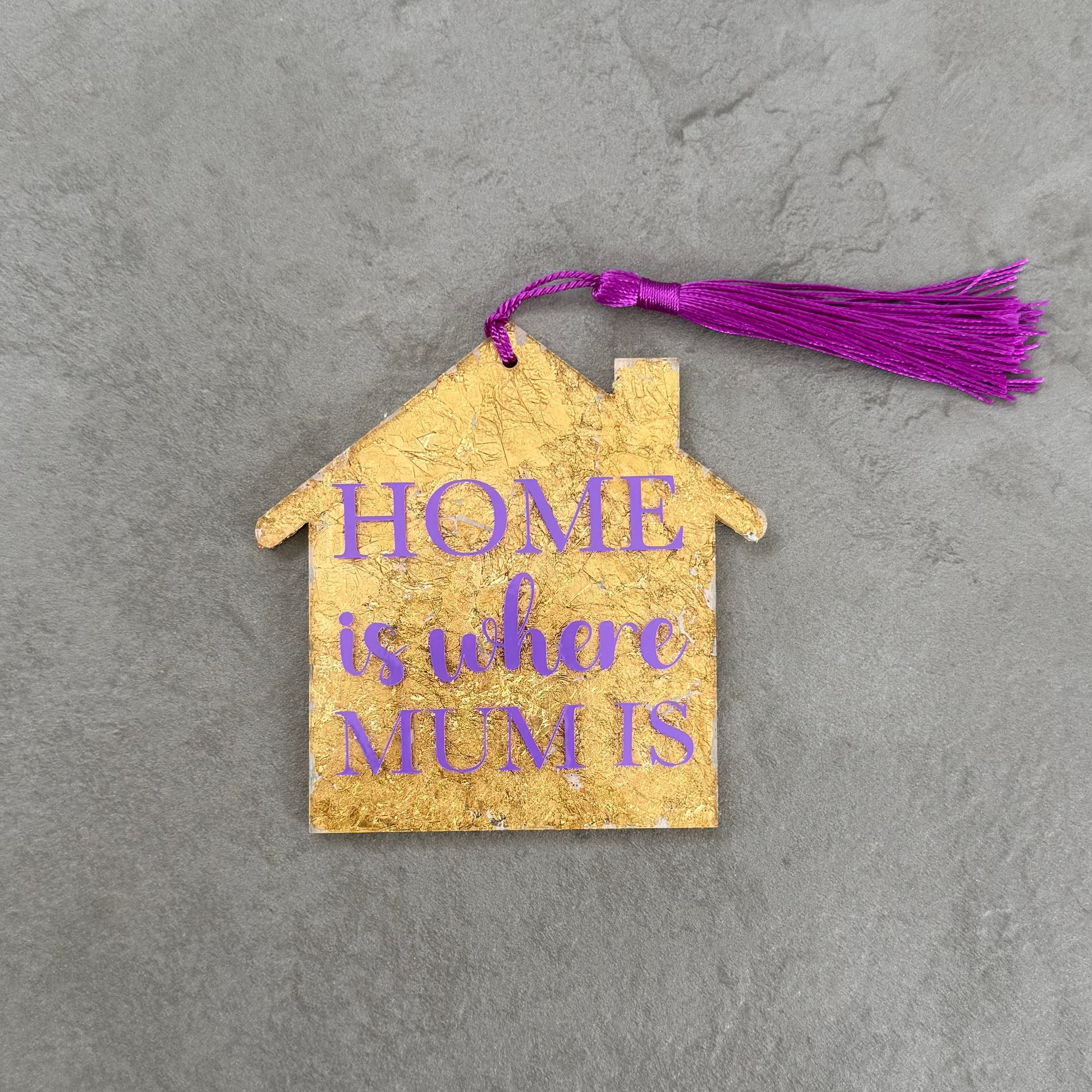 House-shaped wooden ornament with 'HOME is what MUM is' text on a gray surface