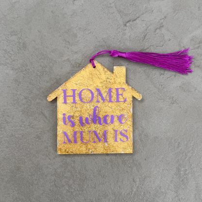 House-shaped wooden ornament with 'HOME is what MUM is' text on a gray surface
