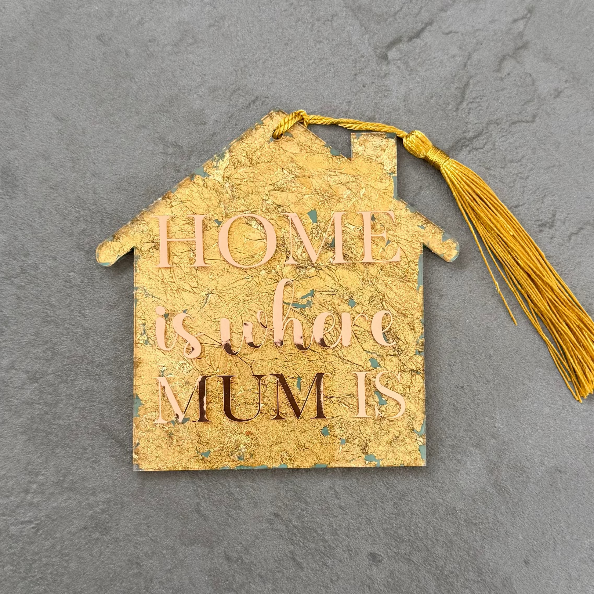 Decorative house-shaped tag with tassel and text on a gray background