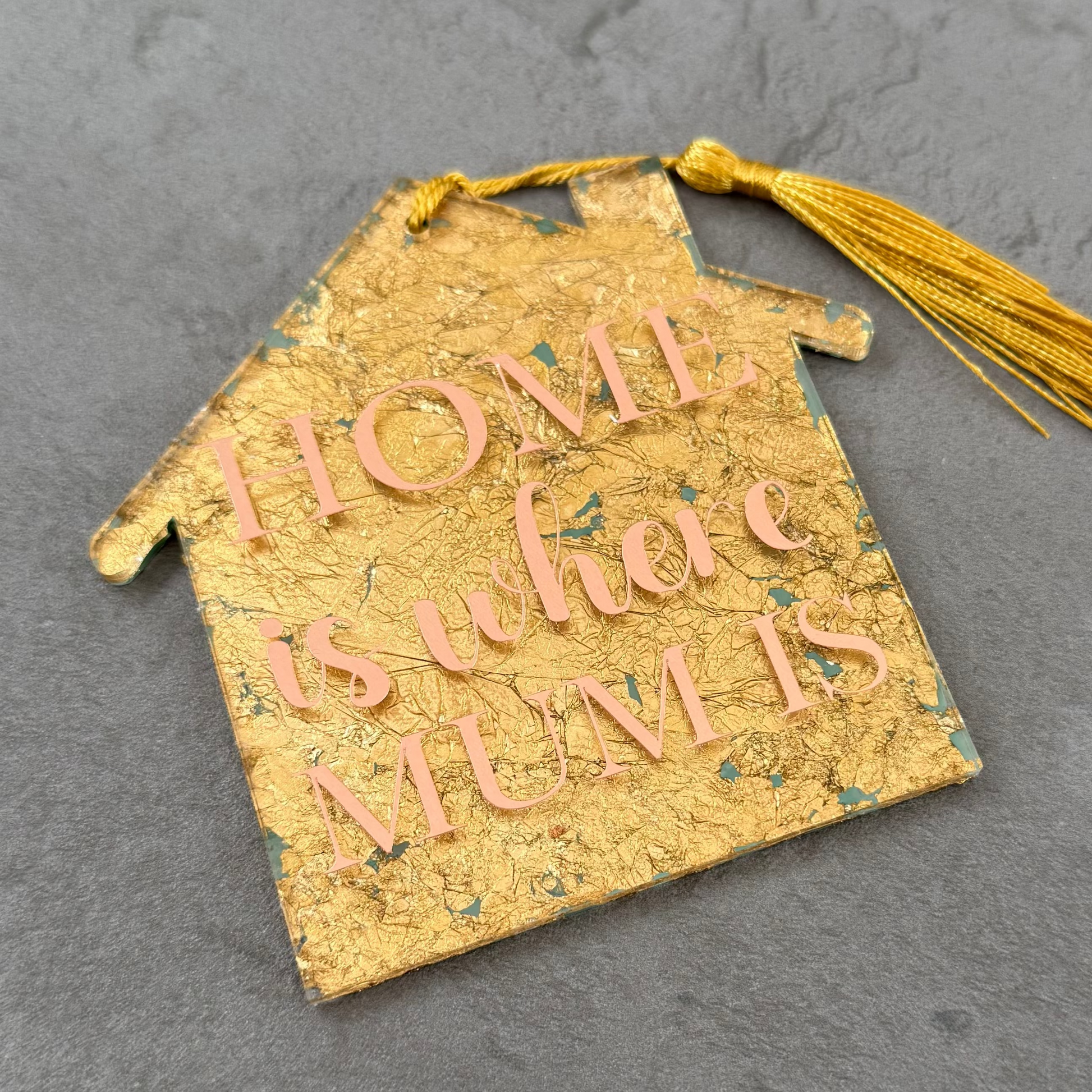 Decorative gold tag with text and tassel on a gray surface