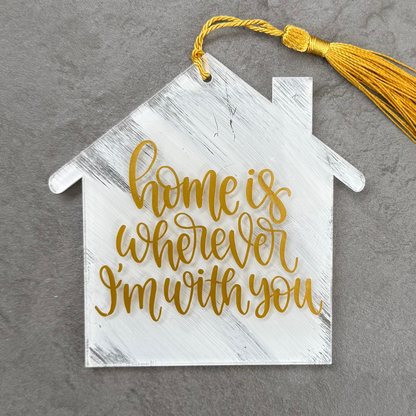 Decorative house-shaped sign with tassel and 'home is wherever I'm with you' text on a gray background