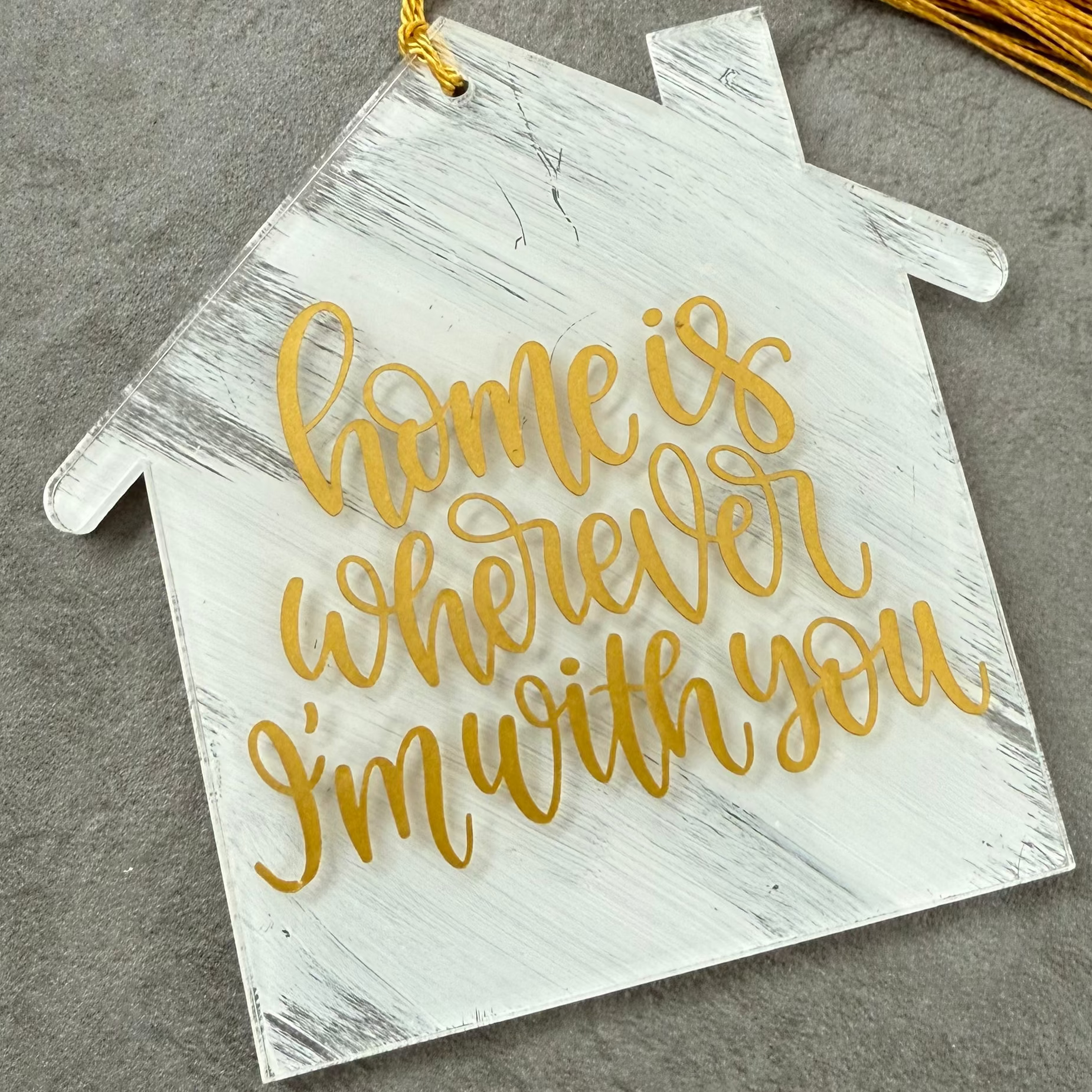 Decorative house-shaped sign with gold text 'home is wherever I'm with you' on a gray background