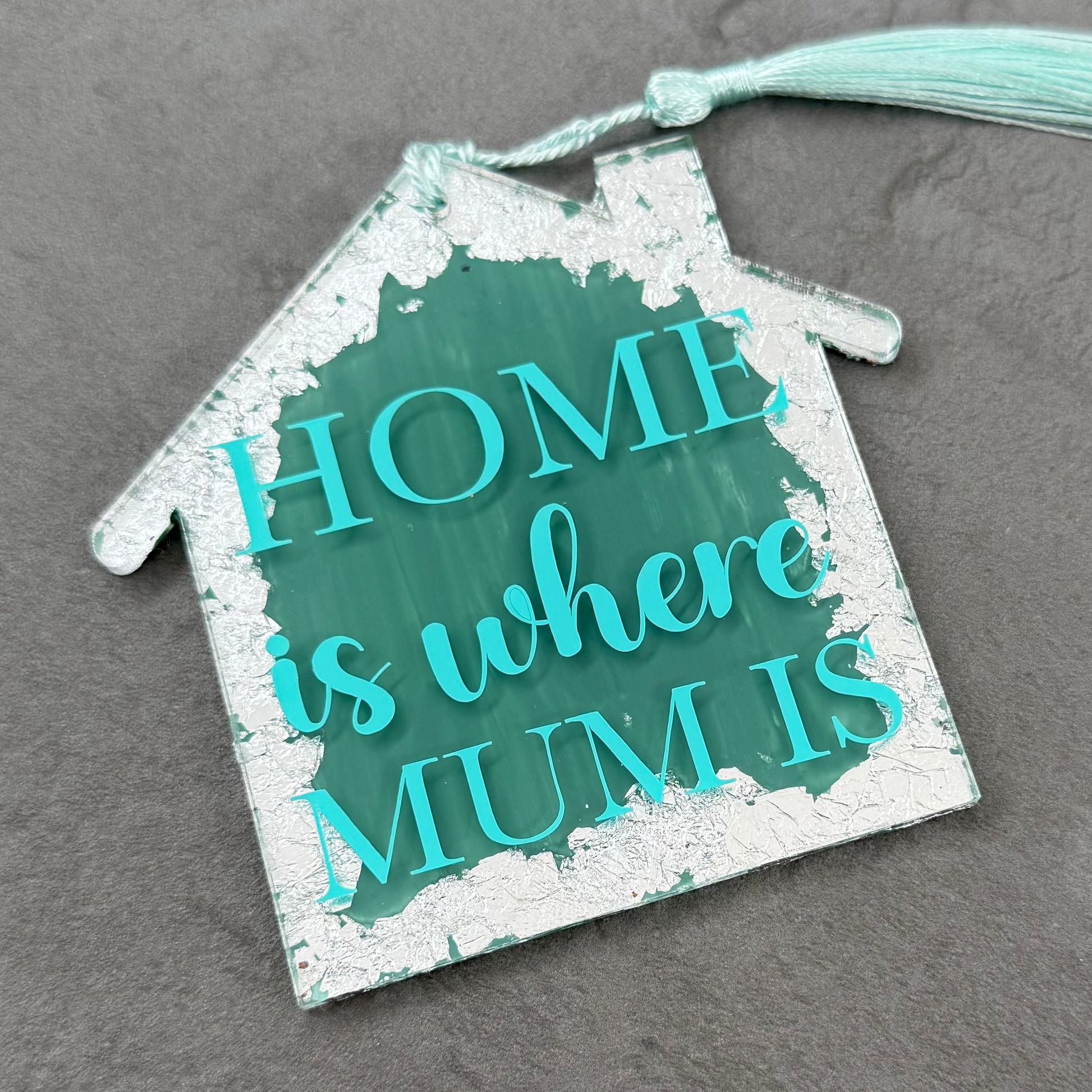 Decorative house-shaped sign with 'HOME is where MUM is' text on a gray surface
