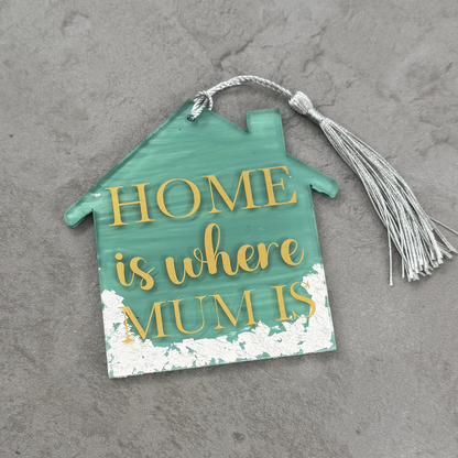 Decorative house-shaped sign with 'Home is where mum is' text on a gray surface