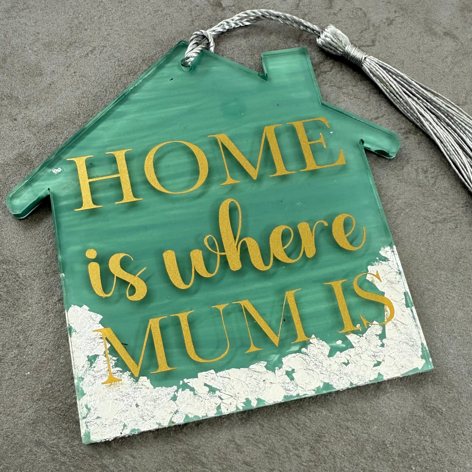 Decorative sign shaped like a house with 'HOME is where MUM is' text on a textured surface.
