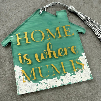 Decorative sign shaped like a house with 'HOME is where MUM is' text on a textured surface.