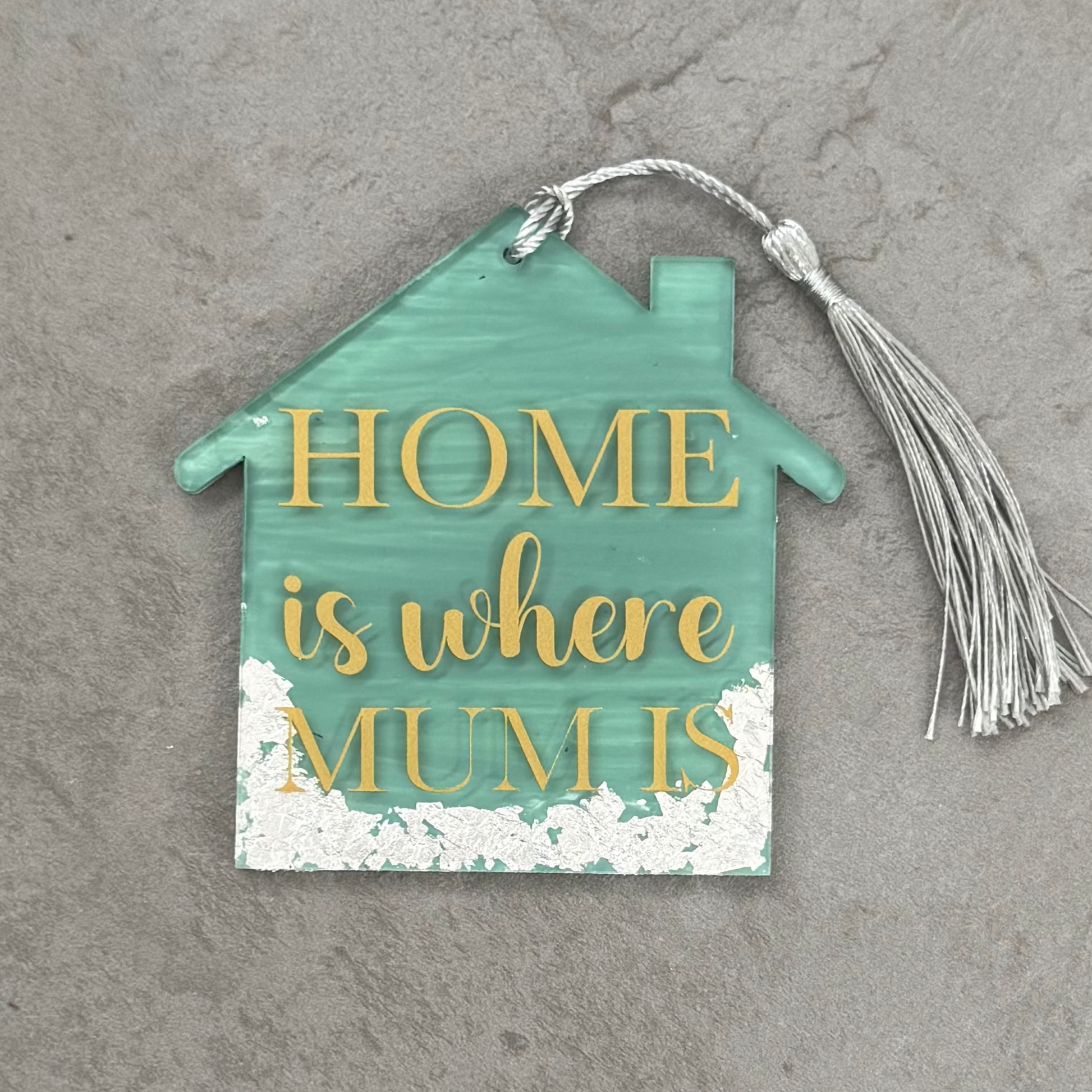 Decorative house-shaped sign with 'Home is where mum is' text on a gray surface