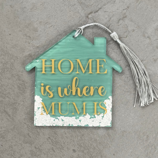 Decorative house-shaped sign with 'Home is where mum is' text on a gray surface