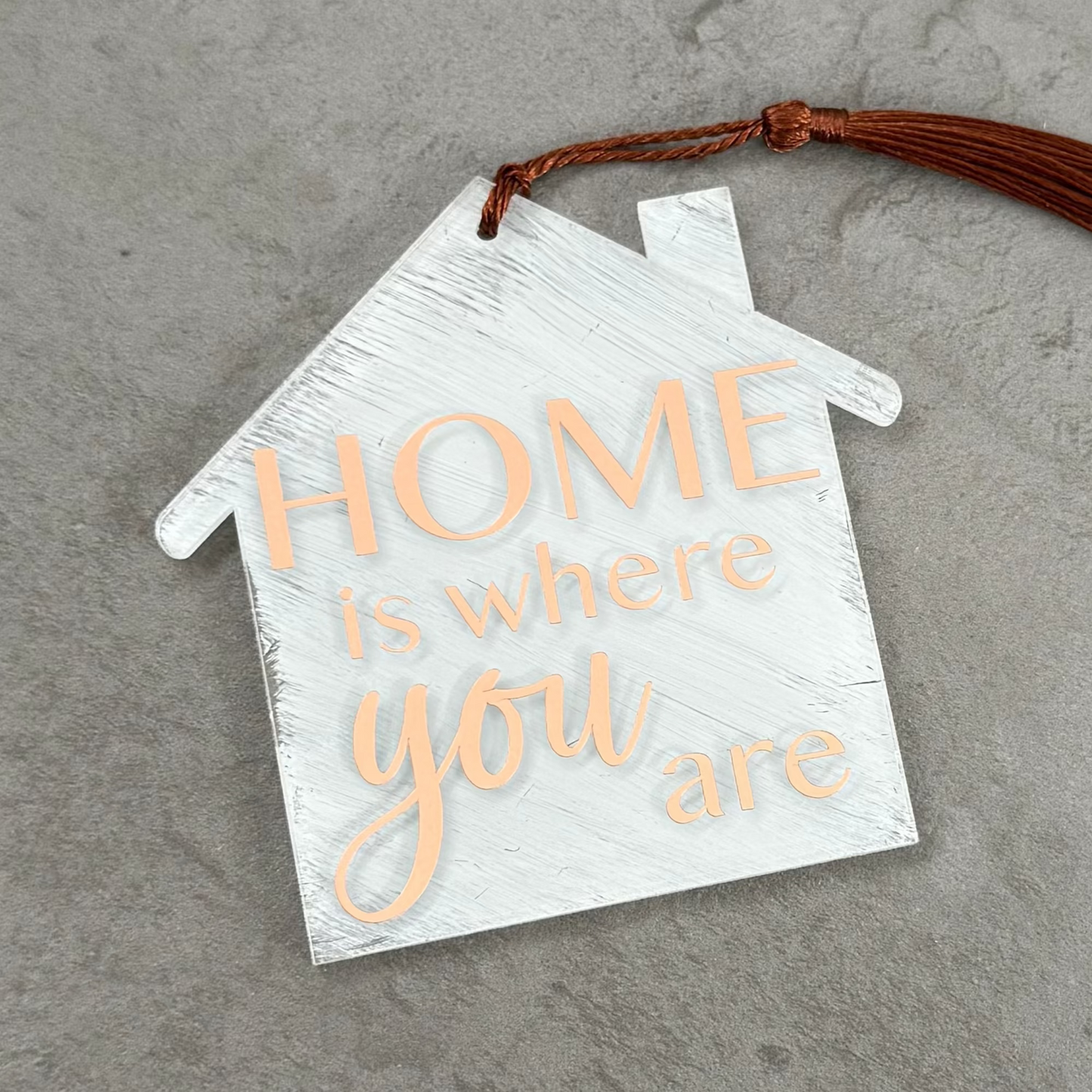 House-shaped sign with 'HOME is where you are' text on a gray surface