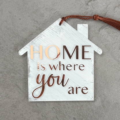 Decorative house-shaped sign with 'Home is where you are' text on a gray surface