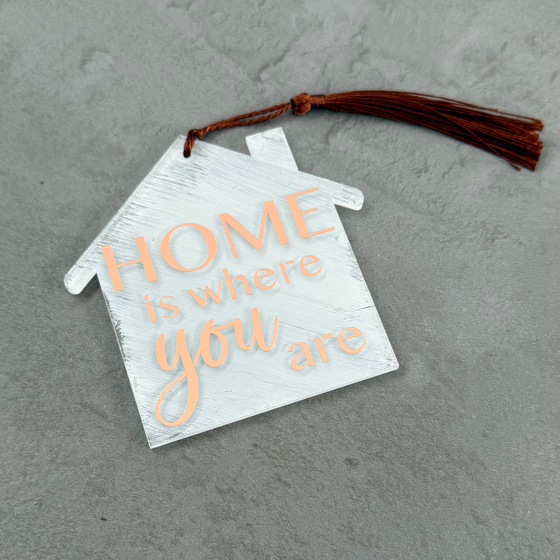 Decorative house-shaped sign with 'HOME is where you are' text on a gray surface