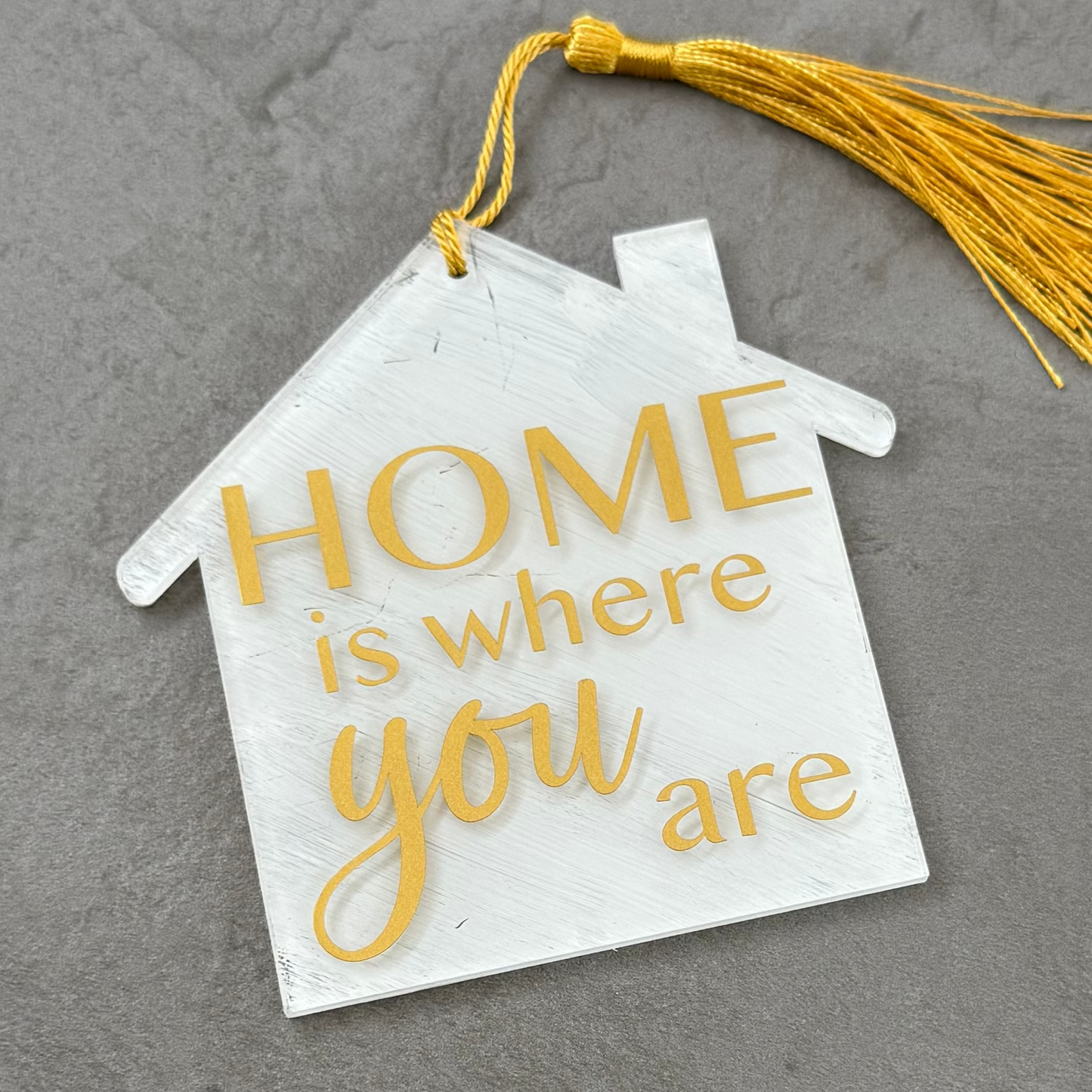 Decorative house-shaped sign with 'HOME is where you are' text on a gray surface