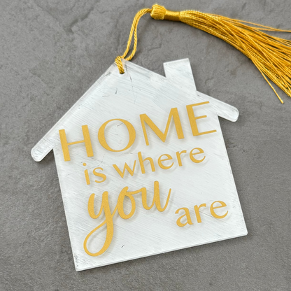 Decorative house-shaped sign with 'HOME is where you are' text on a gray surface
