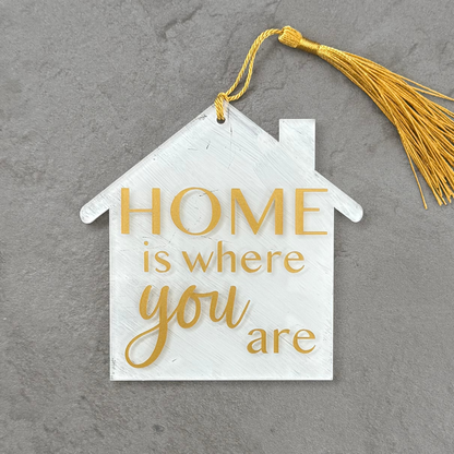 Decorative house-shaped sign with 'Home is where you are' text on a gray background