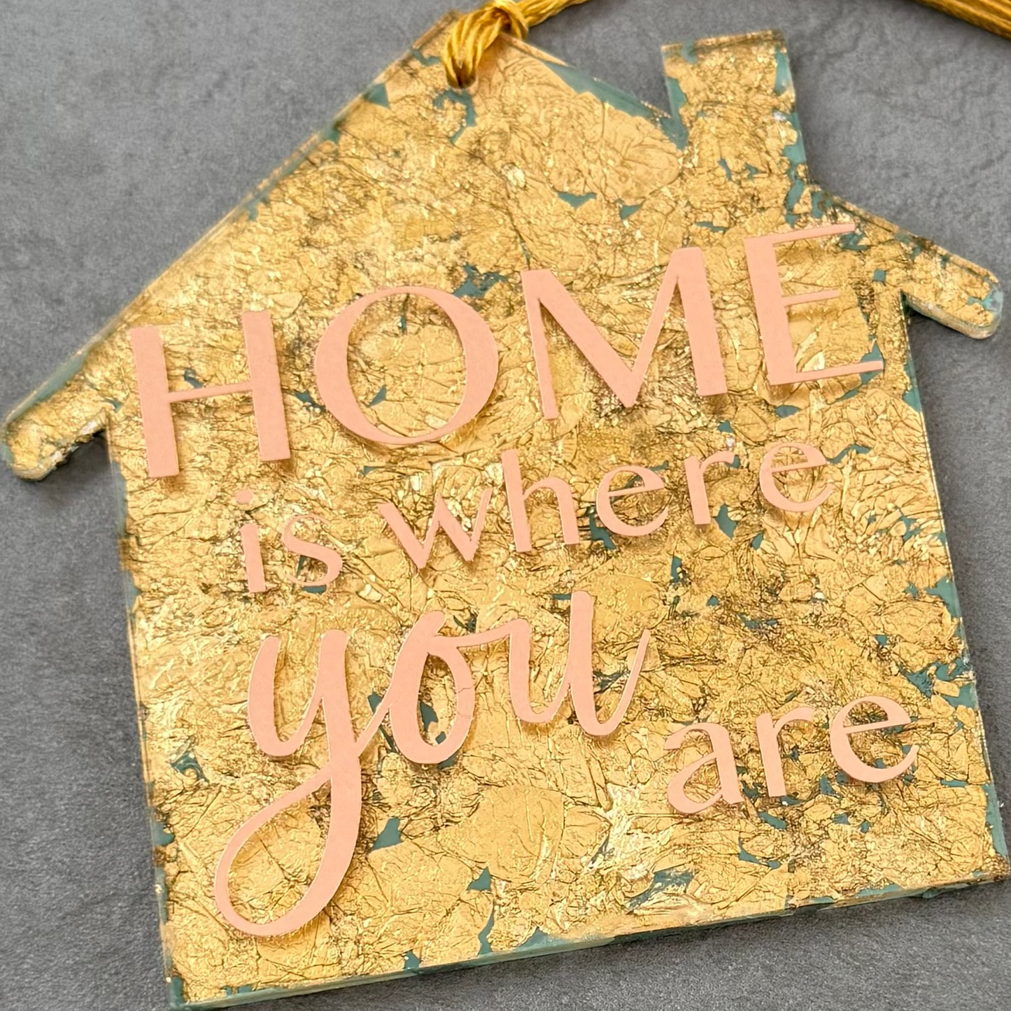 Decorative house-shaped sign with tassel on a gray surface