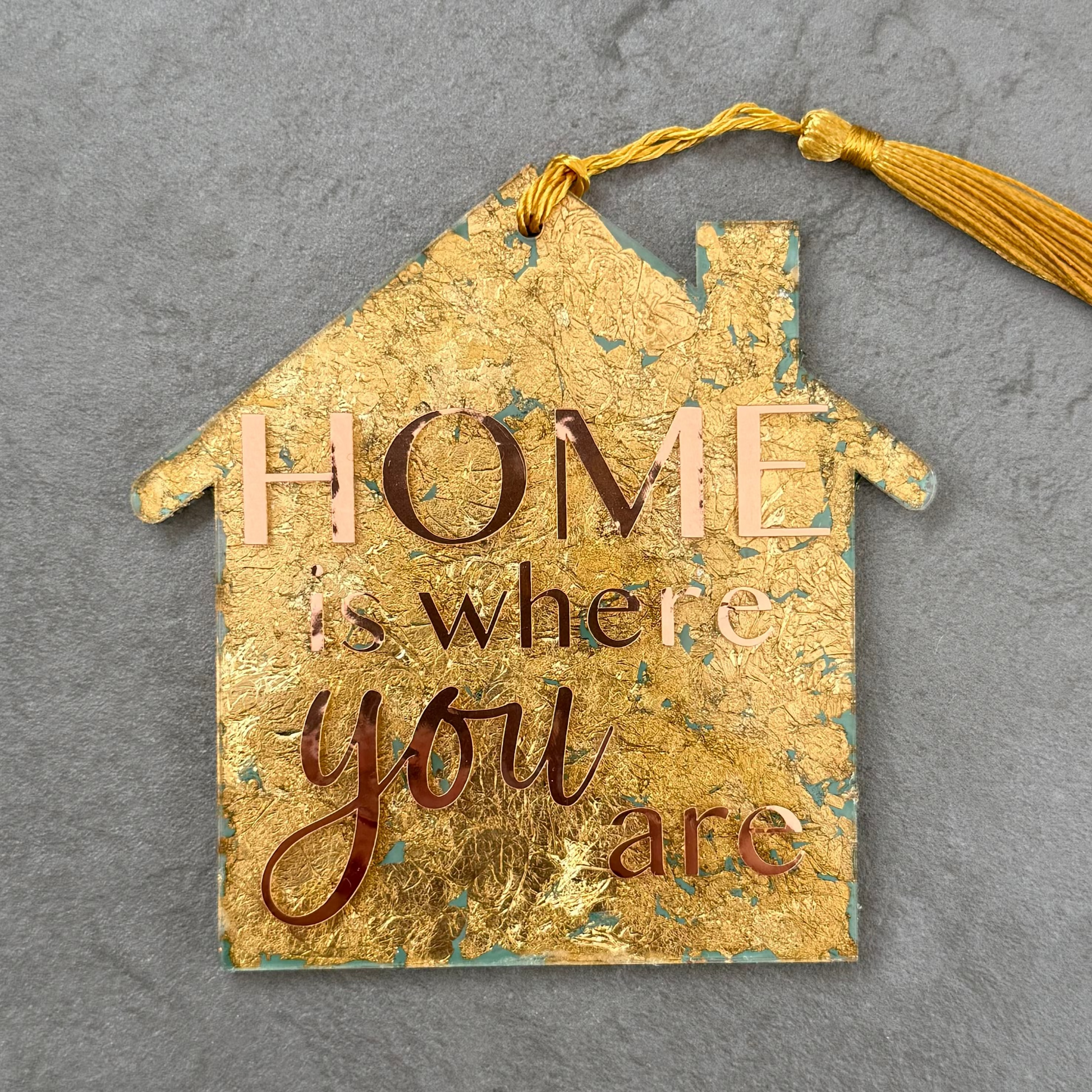 Decorative house-shaped sign with 'Home is where you are' text on a gray background