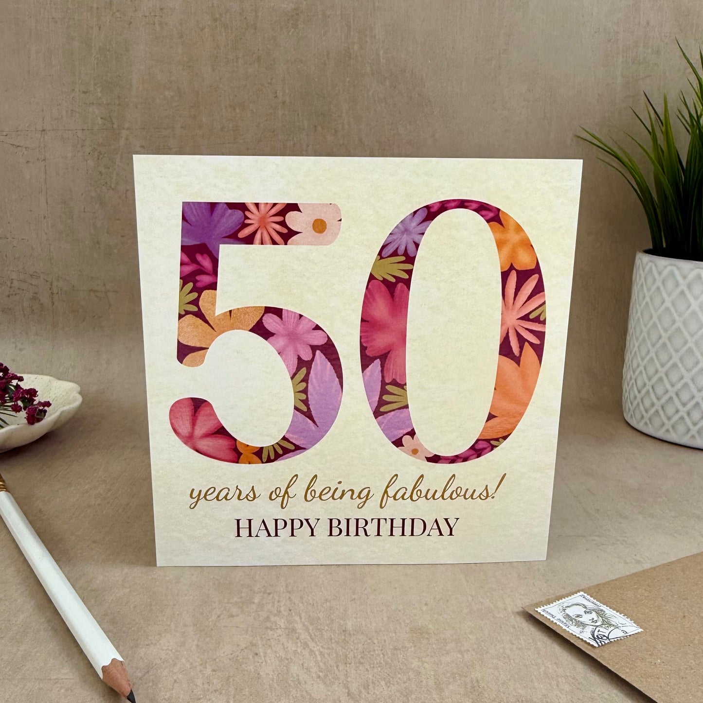 50th birthday card with floral design on a table with a plant and envelope.