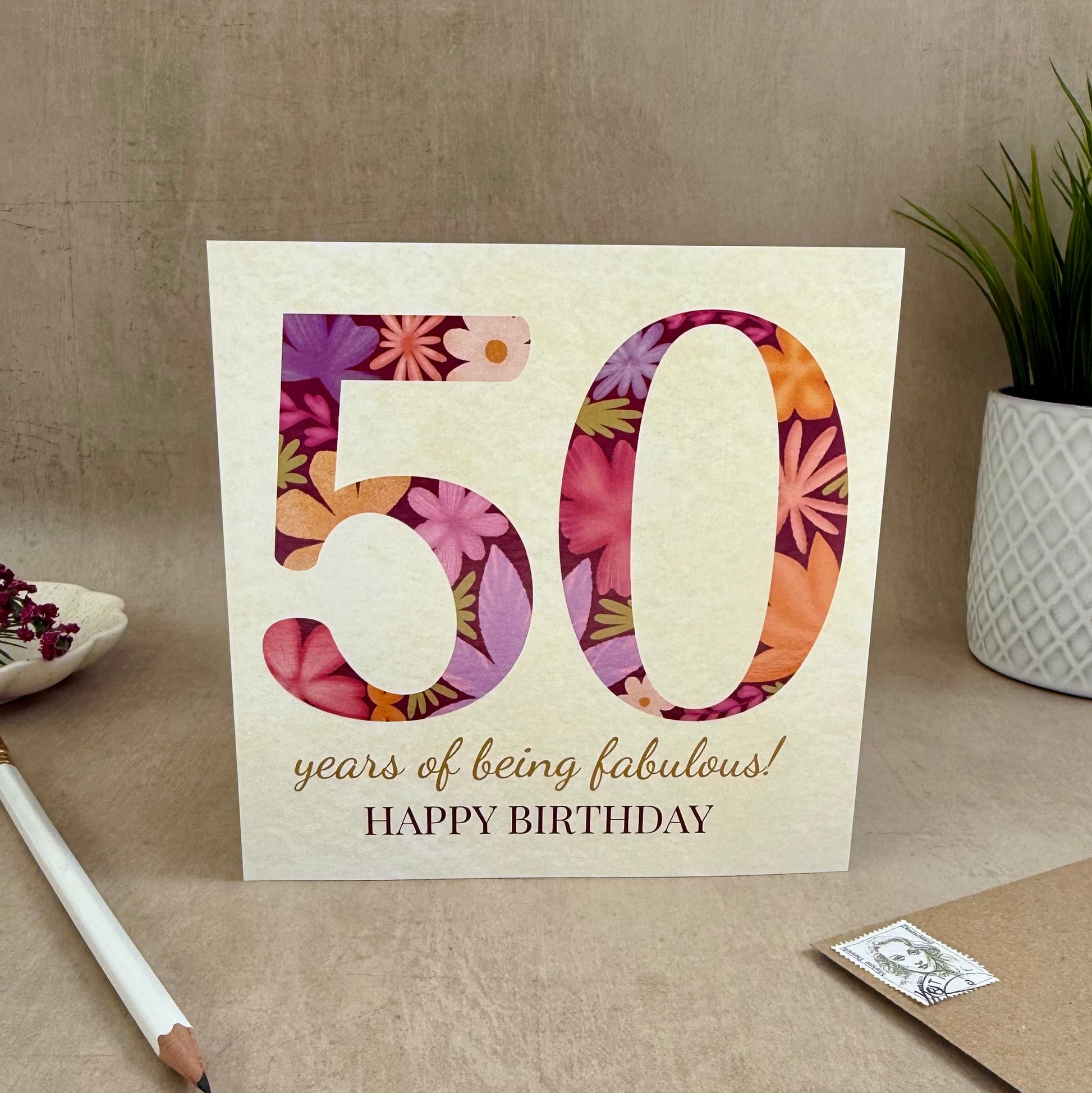 50th birthday card with floral design on a table with a plant and envelope.