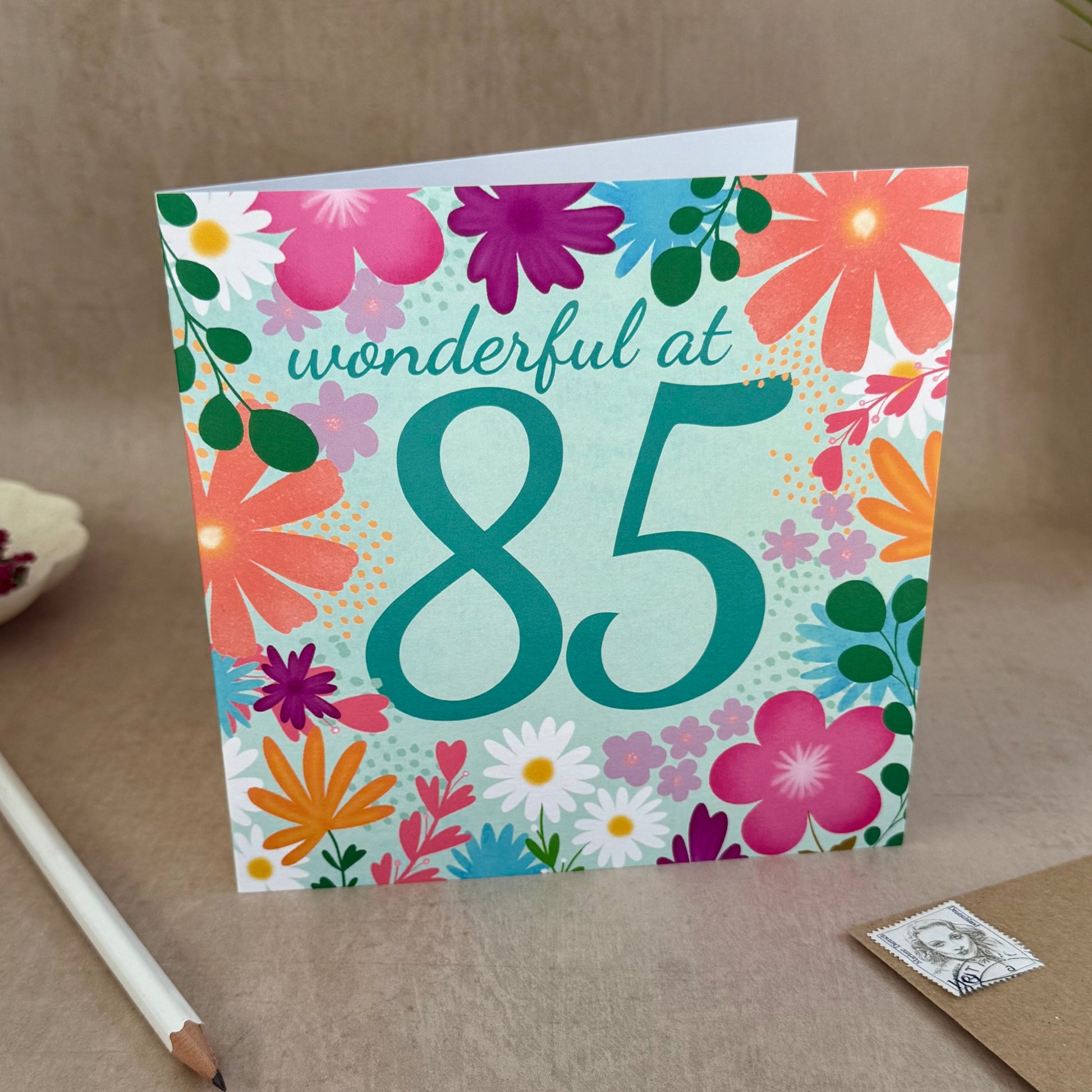 Floral birthday card for someone wonderful at 85 on a desk with stationery items.
