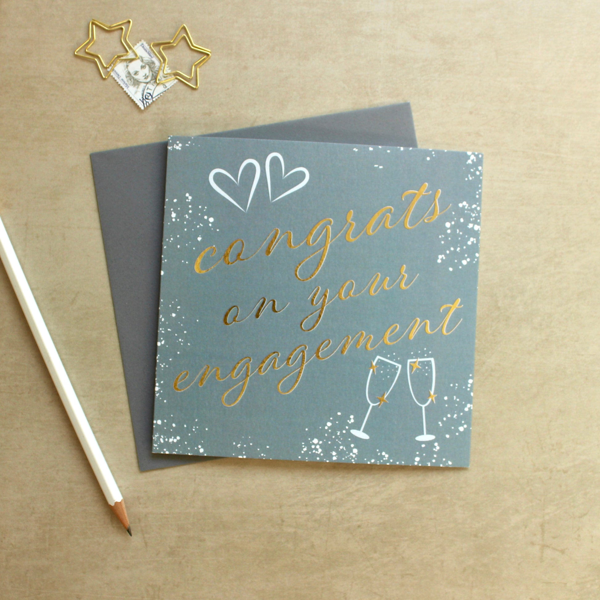 Engagement card with gold text and champagne glasses on a brown background