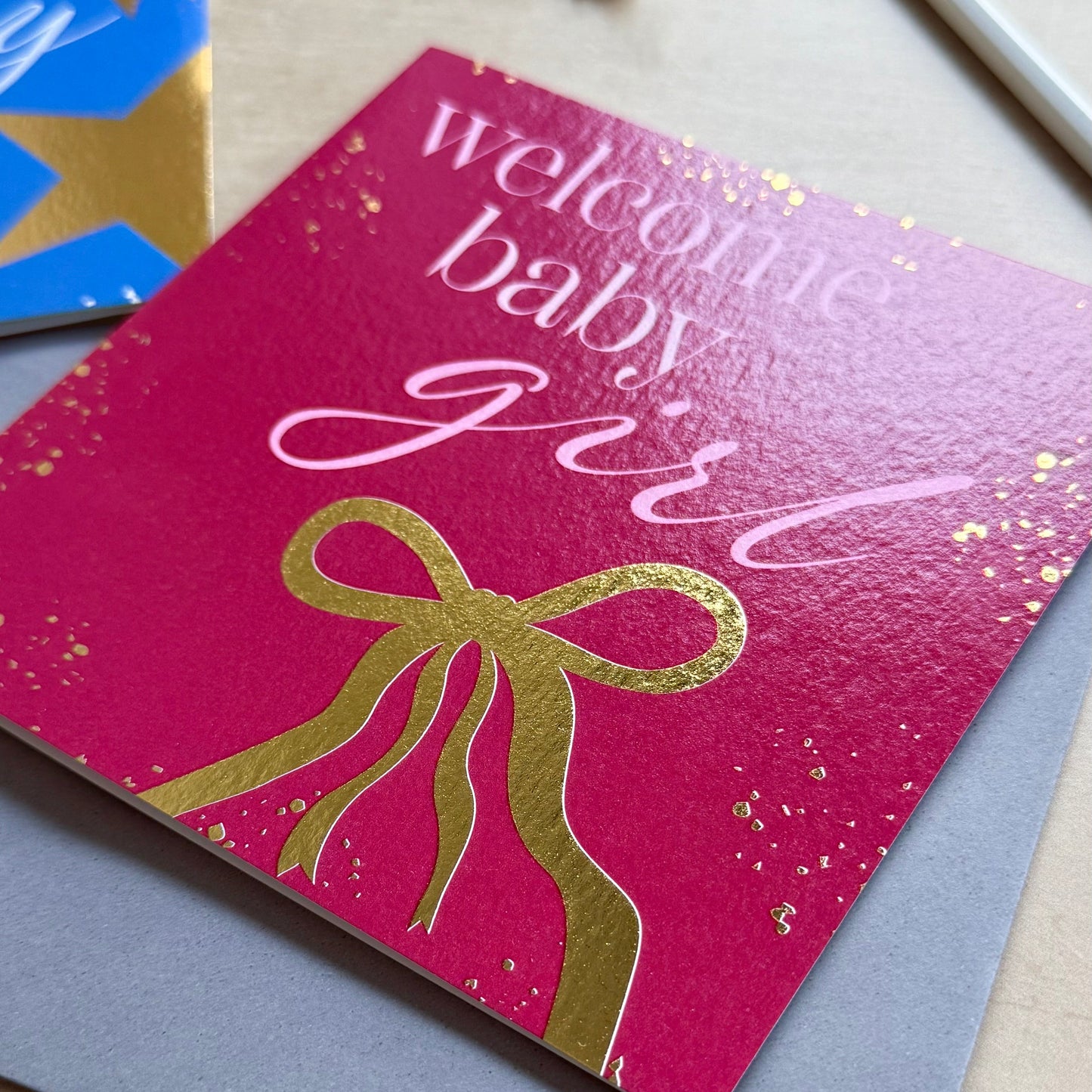 Card with 'welcoming baby girl' text and gold bow design on a pink background.