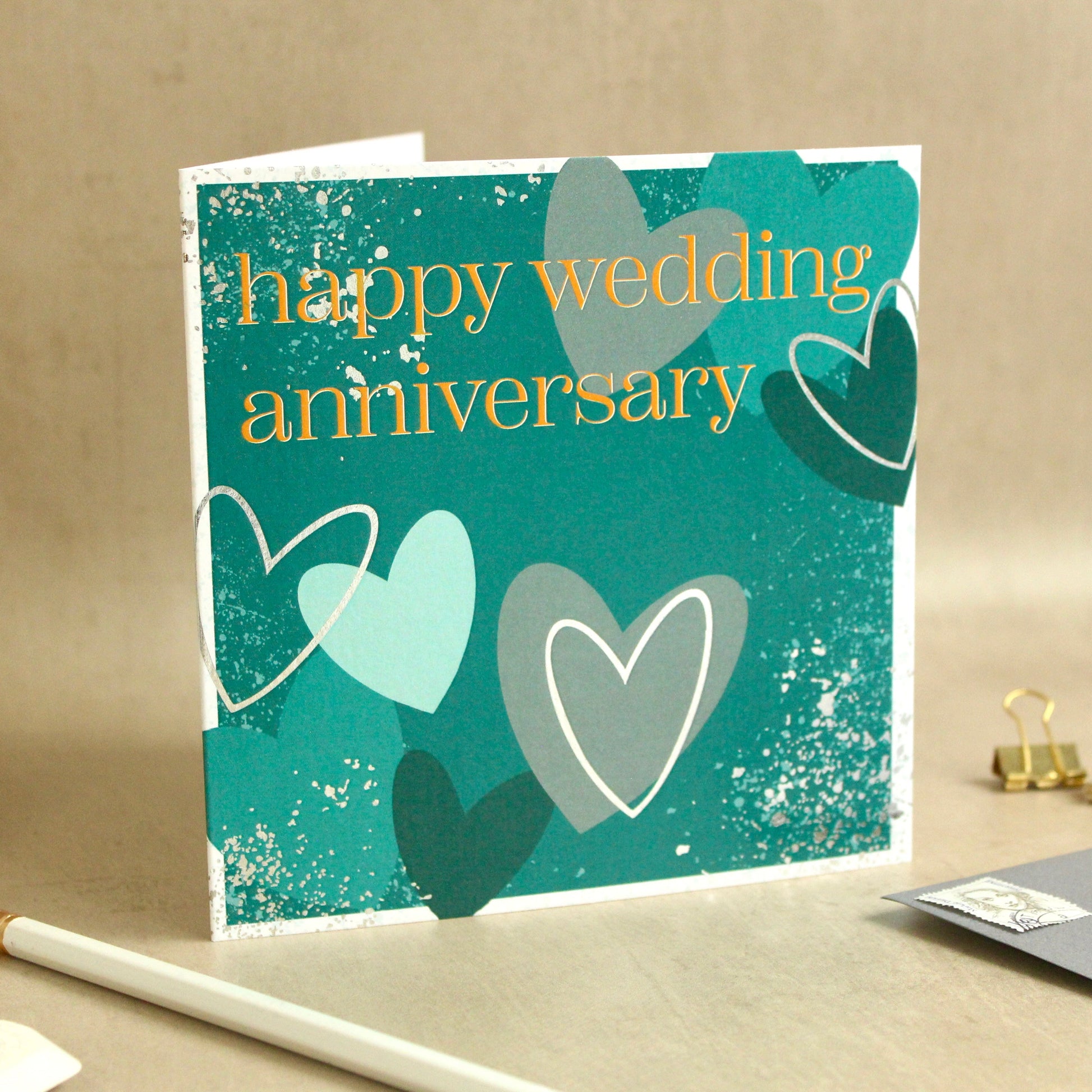 Greeting card with hearts and 'happy wedding anniversary' text on a beige surface.