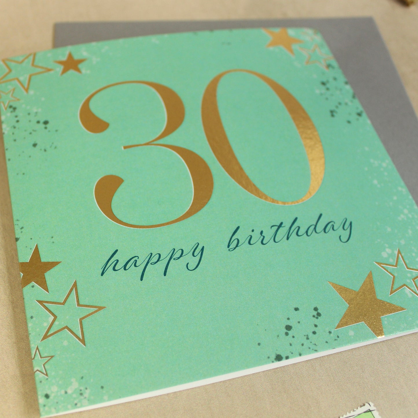 Green birthday card with gold stars and '30 happy birthday' text on a beige surface.