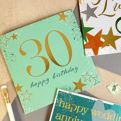 Three greeting cards with '30 happy birthday', 'Good Luck', and 'Happy Wedding Anniversary' text on a beige surface.