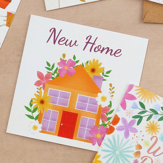 Colorful greeting cards with floral designs and a house illustration on a wooden surface.