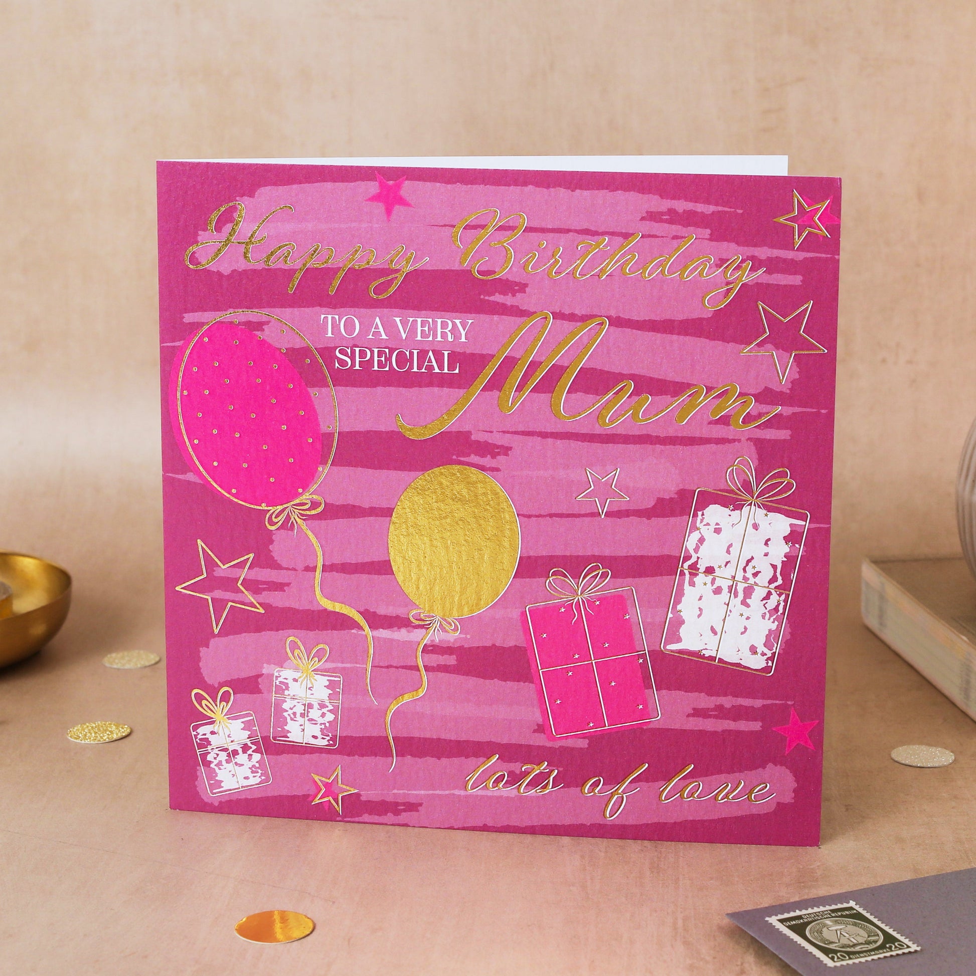 Pink birthday card for a special mum with balloons and presents on a beige surface.