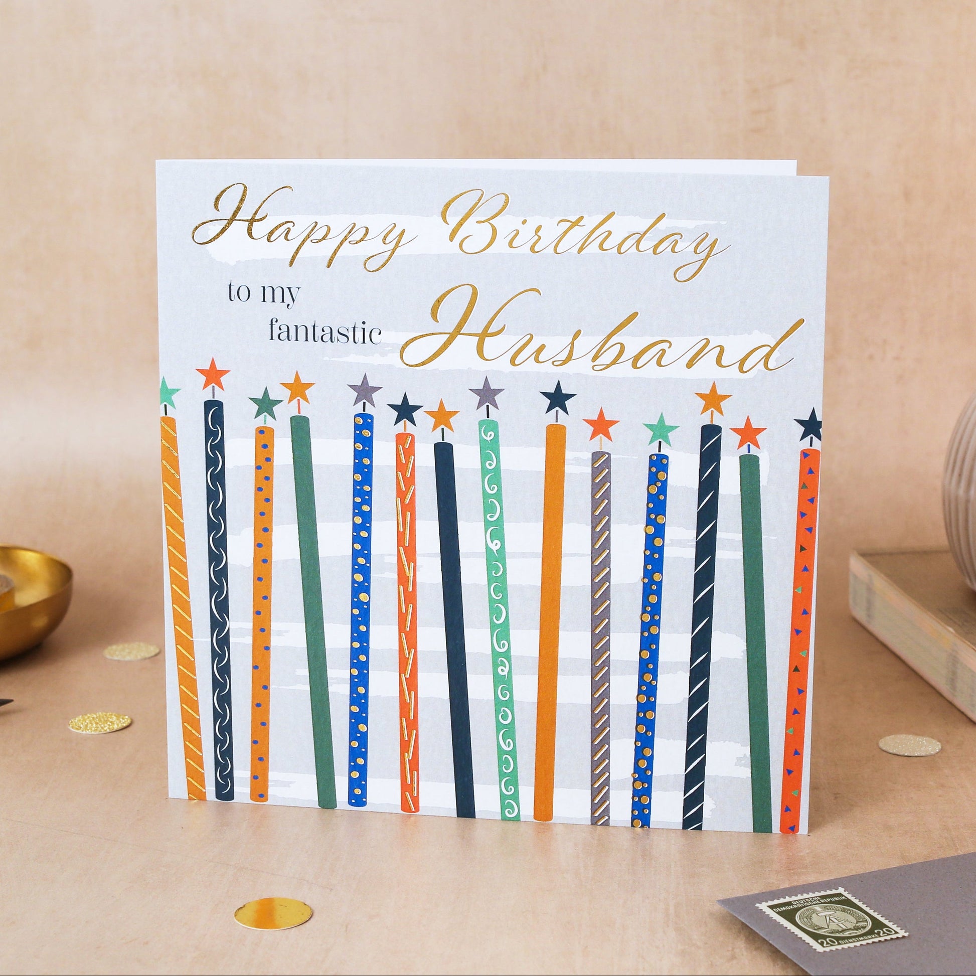 Birthday card for a husband with colorful candles on a wooden surface.