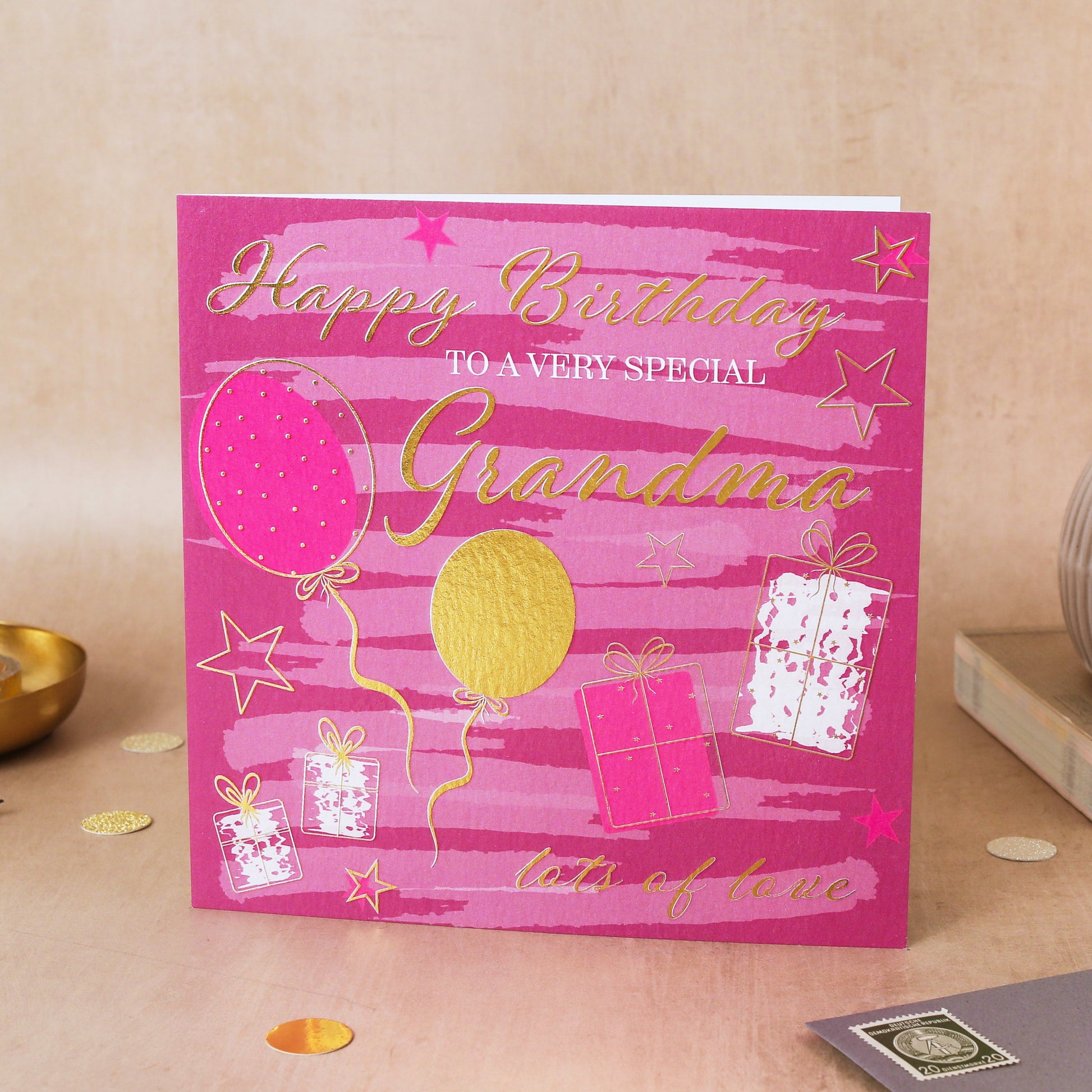 Pink birthday card for a special grandma with balloons and presents on a beige surface.