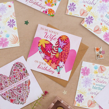 Collection of colorful greeting cards with floral and heart designs on a brown surface.