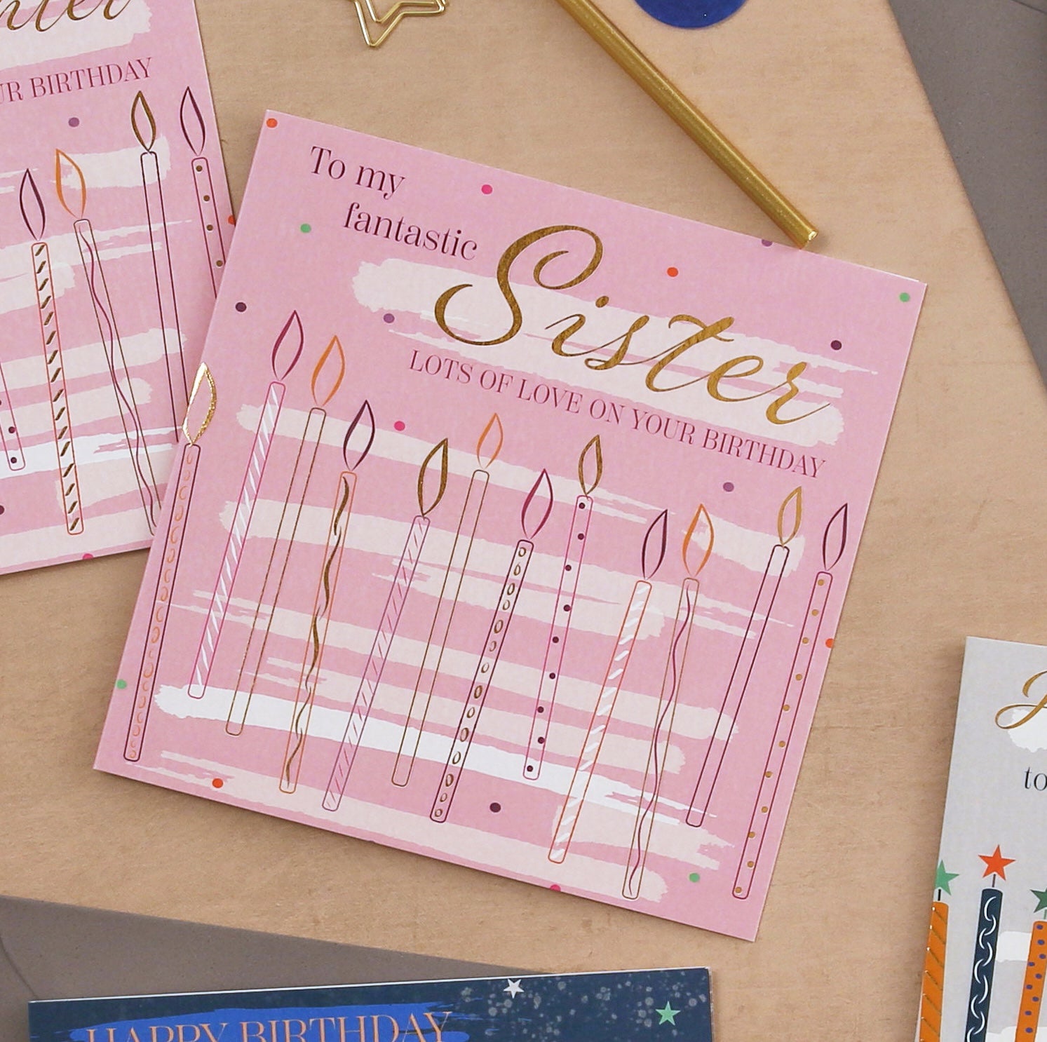 Pink birthday card with candles and 'To my fantastic Sister' text on a wooden surface.